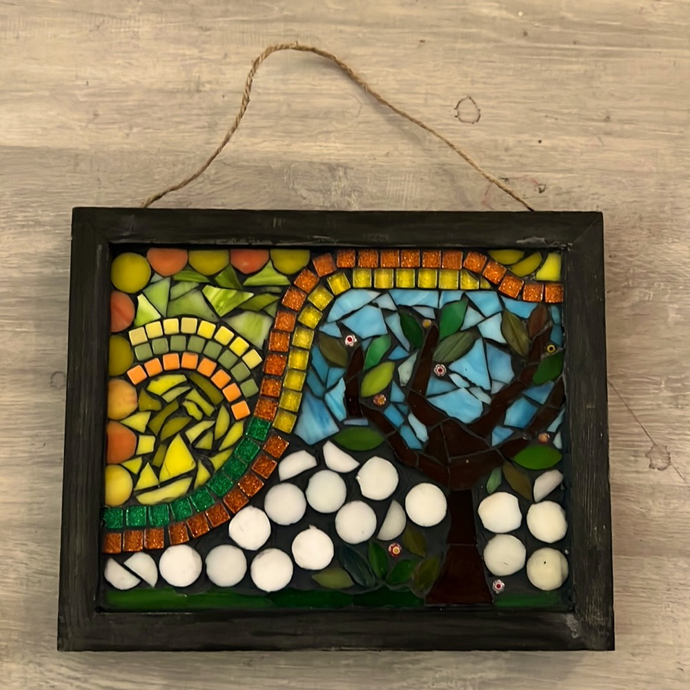 Hanging wall art made of mosaic glass. There is a tree on the bottom right